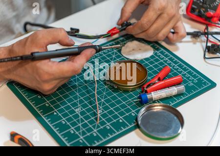 Close-up of hands soldering electronic wires with soldering iron and tools on cutting mat Stock Photo