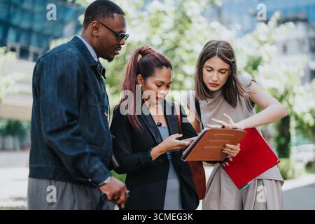 Multiracial colleagues collaborating outdoors with documents and a digital device Stock Photo