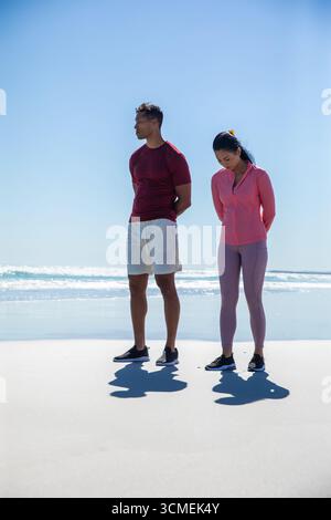 Diverse friends standing on sandy beach feeling ocean waves on wet sand in athletic footwear Stock Photo