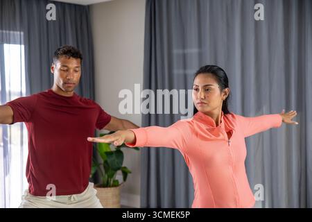 Diverse workout partners practicing warrior ii pose in home living room by plant Stock Photo