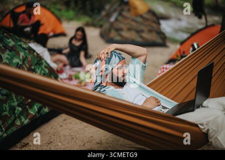 Man relaxing in hammock using a laptop during outdoor camping in nature Stock Photo