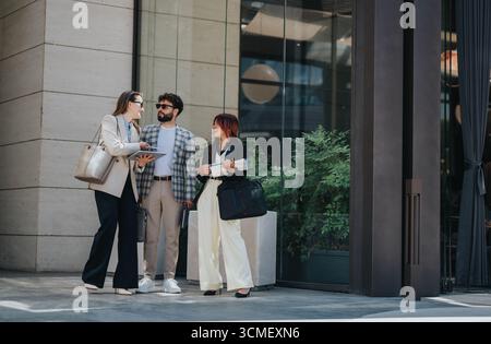 Three colleagues standing outside an office engaged in conversation Stock Photo