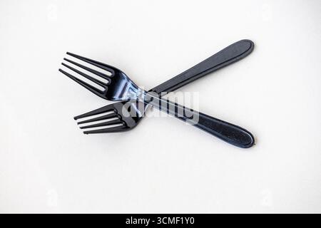 Two black plastic forks, isolated on a white background. These disposable utensils are a global environmental concern, contributing to plastic polluti Stock Photo