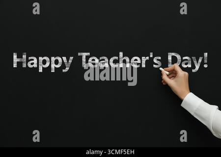 Happy Teacher's Day greeting card. Woman writing text on blackboard, closeup Stock Photo