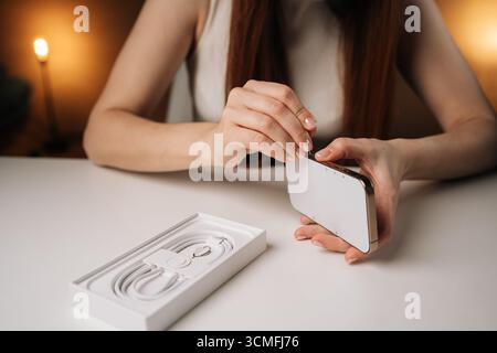Woman inserting metal eject pin into sim card slot of new smartphone, engaging in unpacking process of modern mobile device with precision and care. Stock Photo