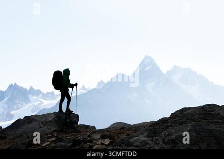 Adventurers silhouette against misty high-altitude snowy peaks. Wilderness and travel inspiration. Backpacker in mountains Stock Photo