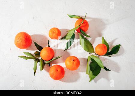 Fresh tangerines with green leaves arranged on textured white background. Top view, flat lay. Stock Photo