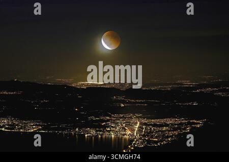 Blood moon, total lunar eclipse over the illuminated city and Lake Zug, Zug, Canton Zug, Switzerland Stock Photo