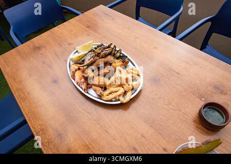 Assorted fried seafood platter with shrimp, calamari rings, fish, and mussels served with lemon on a wooden table. Traditional Canary Islands cuisine, Stock Photo