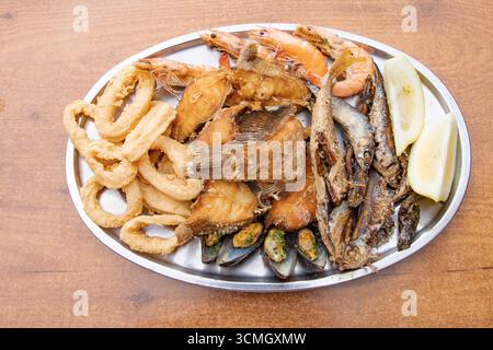 Assorted fried seafood platter with shrimp, calamari rings, fish, and mussels served with lemon on a wooden table. Traditional Canary Islands cuisine, Stock Photo