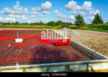 Red underfloor heating pipes laid in reinforced concrete slab foundation with insulation, prepared for radiant floor heating system in new constructio Stock Photo