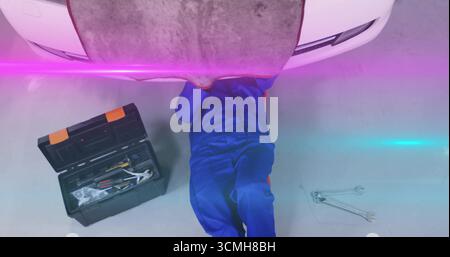 Repairing mechanic checking underside of white car on workshop floor, with toolbox and wrenches Stock Photo