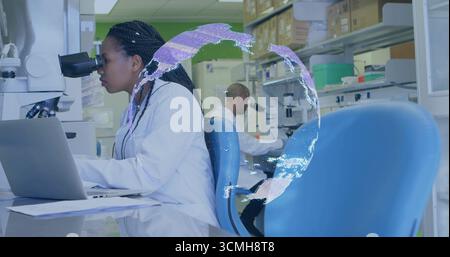 Examining woman scientist in lab coat operating microscope, using laptop at lab bench, copy space Stock Photo