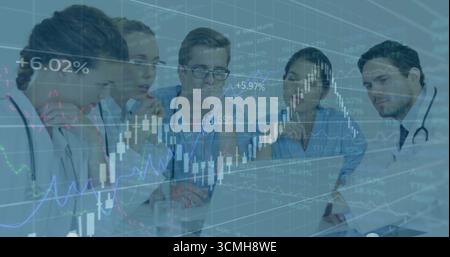 Reviewing medical team in scrubs analyzing charts on laptop in meeting room, candlestick graphs Stock Photo