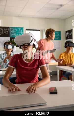 Chinese woman student sitting at desk wearing VR headset in classroom with teacher holding tablet Stock Photo