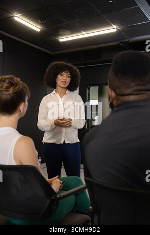 Diverse coworkers sitting with water bottle and listening to facilitator speaking in meeting room Stock Photo