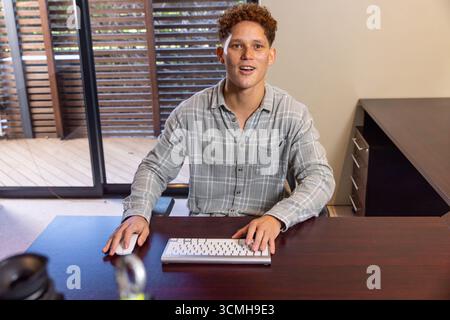 Man typing on white keyboard and using mouse at office desk by sliding glass doors Stock Photo