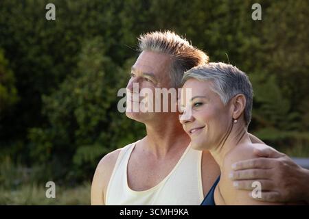 Senior couple standing closely together in backyard garden under afternoon sunlight Stock Photo
