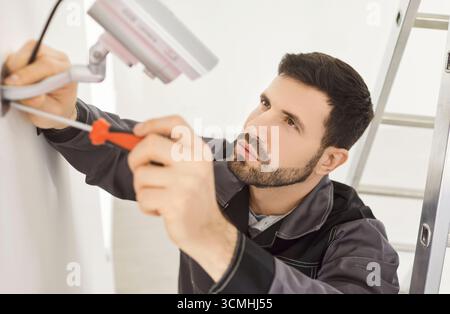 Serious man working in security company, screwing CCTV camera on wall installing surveillance system Stock Photo
