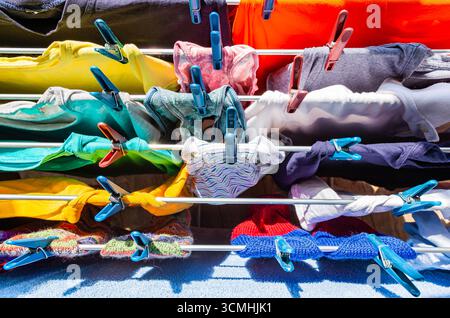 Multi-colored clothes hang attached to clothespins and dry after washing, close-up. Stock Photo