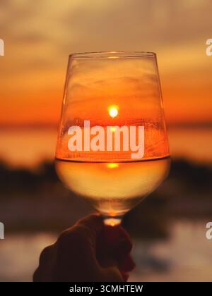 The setting sun reflects in a glass of white wine Stock Photo