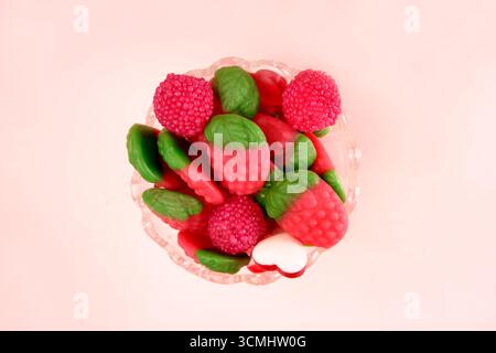 Small glass bowl full of colorful gummy candy shaped like strawberries and raspberries, sitting on a pink background Stock Photo