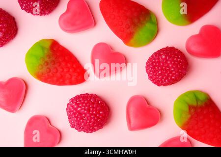 Delicious gummy candies shaped like hearts, strawberries, and raspberries creating a vibrant pattern on a pink background Stock Photo