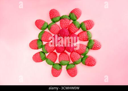 Colorful strawberry shaped gummy candy forming a circle on a pink background, with small round candies and a heart shaped candy in the center Stock Photo