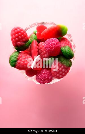 Glass bowl full of sweet, colorful gummy candy in fruit shapes, sitting on a pink background Stock Photo