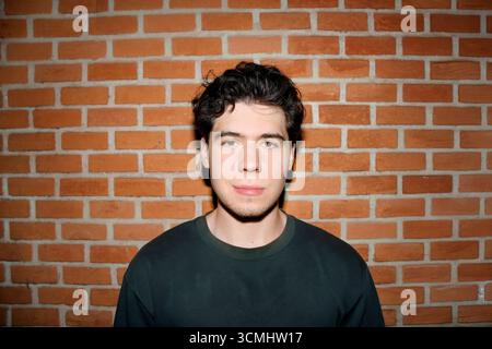 Portrait of a young man standing against a brick wall Stock Photo