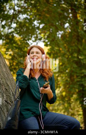 Happy businesswoman enjoying music with headphones and smartphone in a green park during a break Stock Photo