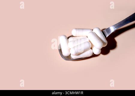 White pills resting on a spoon against a pink backdrop, symbolizing medicine, healthcare, and pharmaceutical concepts Stock Photo