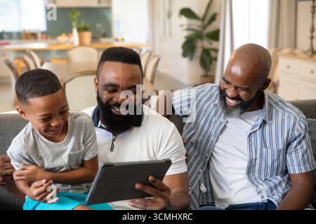 African American family sharing digital tablet and laughing on gray sofa in open-plan living area Stock Photo