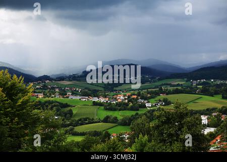 Green valley landscape with village houses and storm clouds forming over distant hills. Stock Photo