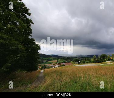 Storm clouds rolling over rural bavarian fields with farms and hills in the distance. Stock Photo