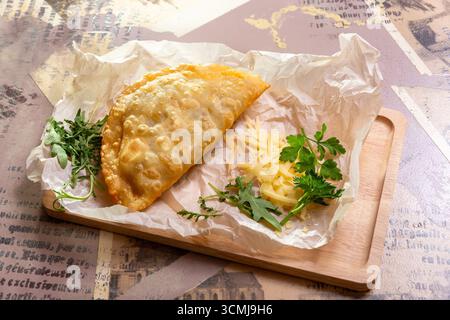 Golden brown cheburek pastry with cheese and arugula on rustic wood board. Food flat lay on craft paper. Stock Photo