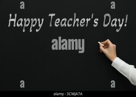 Happy Teacher's Day greeting card. Woman writing text on blackboard, closeup Stock Photo