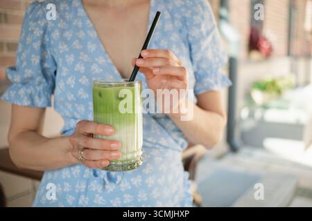 Close-up of a woman in a summer dress standing outdoors drinking an iced matcha latte Stock Photo