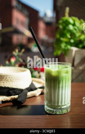 Close-up of an iced matcha latte and a straw sun hat on a cafe table in summer Stock Photo