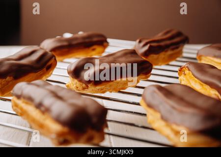 Freshly baked chocolate eclairs cooling on a rack in natural warm light Stock Photo