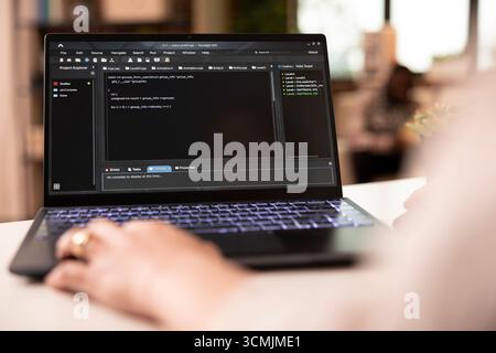 Closeup of programmer working from home, typing and debugging software code for app development. Young adult freelancer focused on project for tech company in apartment workspace. Stock Photo