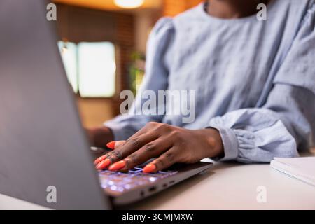 Closeup of female financial advisor working from home, seated in cozy living room and typing reports on laptop. Professional woman writing financial updates while managing tasks remotely. Stock Photo