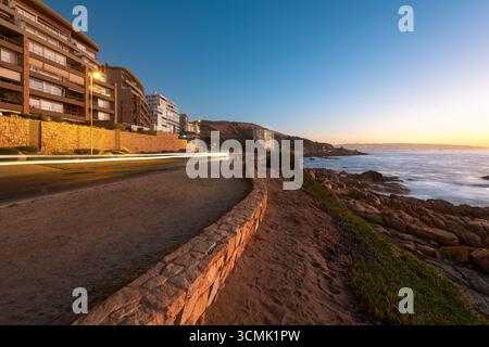A view of a coastal road in Concon, with the ocean and rocks illuminated by the last light of day. Stock Photo