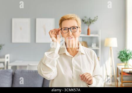 Stylish, beautiful mature woman adjusts her glasses, emphasizing her elegant demeanor. Stock Photo