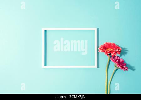 Picture frame with pink and orange gerbera flowers on turquoise background. Top view, flat lay, mockup. Stock Photo