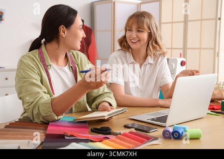Female tailors working with notebook and laptop at table in atelier Stock Photo