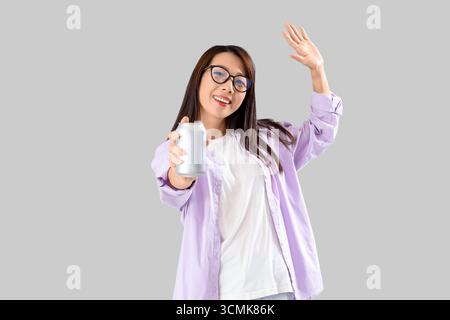 Young Asian woman with drink on grey background Stock Photo