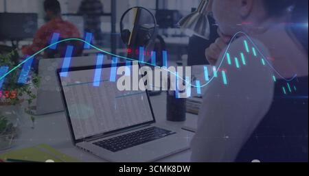 Analyzing spreadsheet woman wearing dark top working at open-plan office, with laptop, stock charts Stock Photo