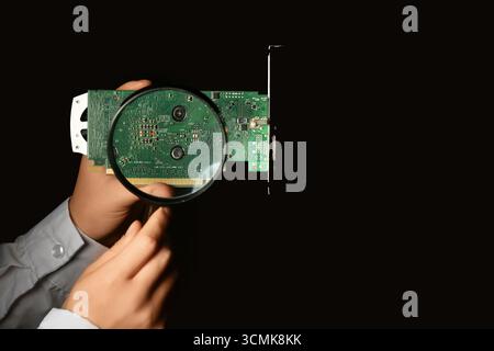 Young woman with magnifying glass examining video card on black background. Inventor concept Stock Photo