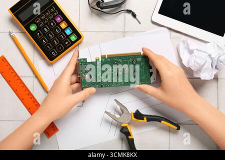 Young woman with video card, crumpled paper, schematics and calculator on table. Inventor concept Stock Photo